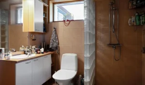 A narrow but beautifully organized small bathroom showing a clear walking path between the entrance, vanity, toilet, and shower. Warm natural light