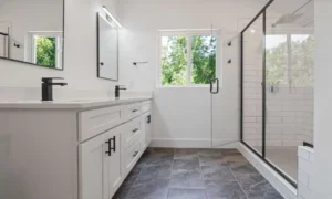 A well-designed small bathroom demonstrating smart layout choices — wall-mounted vanity, glass shower enclosure, clear sightline to a window or mirror, and visible open floor space. Warm, realistic, editorial style